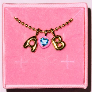 Dettaglio collana dorata con ciondolo a cuore e lettere in astuccio rosa
