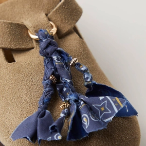 Gros plan d'une chaussure en daim marron avec gland tissé floral bleu et détails dorés