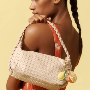 Detalle del bolso tejido beige con colgantes de ganchillo de limón y naranja por modelo