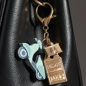 Detalle de llavero de moto azul con placa grabada de Milán en bolso de cuero negro