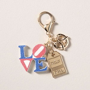 Detalle de colgante LOVE de cuero y placa Philly en accesorio de bolso dorado