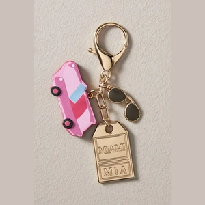 Detalle de un llavero dorado con placa Miami grabada, autobús rosa y gafas de sol