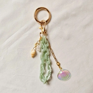 Detail view of gold keychain with ocean-style shell charms and green acrylic chain links