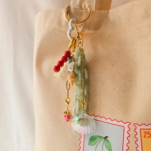 Detail of 18K gold plated keychain with red beads and shells on a canvas bag