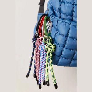 Detail of colorful braided paracord keychains with carabiners on a blue quilted bag