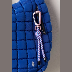 Close-up of electric blue quilted nylon bag with pink carabiner and woven cord detail