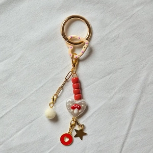 Detail of 18K gold plated keychain with red mushroom bead and pink heart charms