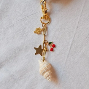 Detail view of gold keychain with cactus, star, cherry charm and a white natural seashell