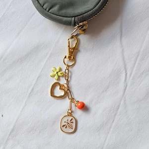 Detail of 18K gold-plated keychain with floral and bee charms on a nylon coin purse
