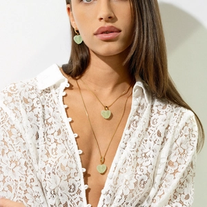 Dettaglio del set di collana e orecchini a cuore dorati indossati su camicia in pizzo bianco