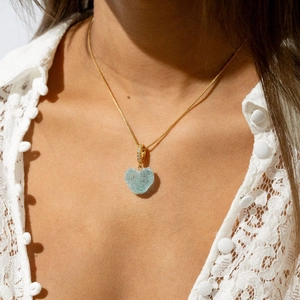 Detalle del colgante de corazón azul claro con cadena dorada sobre modelo