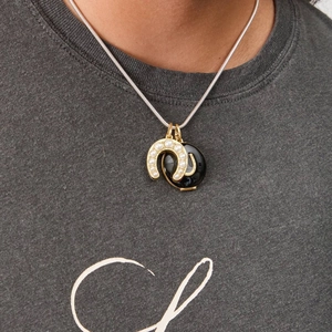 Detailed close-up of a horseshoe pendant with pearls and black oval charm on a chain