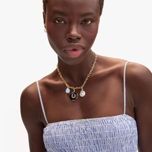 Detail of gold necklace with blue bead, horseshoe charm and irregular pearl on model