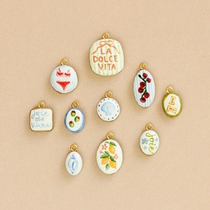 Piatto di 10 ciondoli artistici con frutta e anelli placcati oro 18K su carta beige chiaro