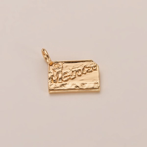 Detalle de un colgante MetroCard dorado con letras en relieve y textura industrial vintage