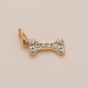 Primer plano de colgante de hueso dorado con pedrería para collar o accesorio mascota