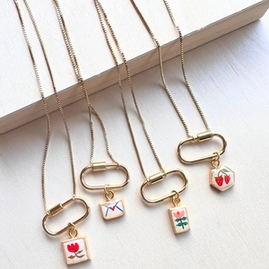 Detailed close-up of 18K gold plated flower and fruit charms on square enamel pendants