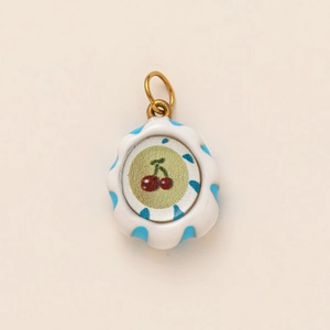 Detailed view of a round cherry charm with blue stripes and gold metal ring attachment