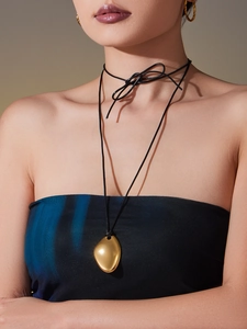 Détail du collier avec pendentif géométrique doré et cordon en cuir noir à effet miroir
