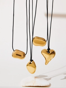 Détail de pendentifs dorés organiques et de breloques en cœur sur cordons noirs