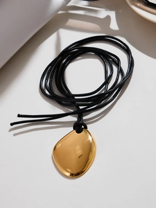 Vue macro du pendentif géométrique doré irrégulier avec finition miroir et cordon