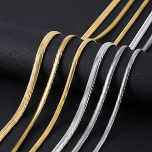 Close-up of gold and silver stainless steel flat snake chains on a black leather stand
