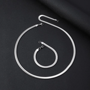 Polished silver flat snake chain necklace and bracelet set on black textured surface