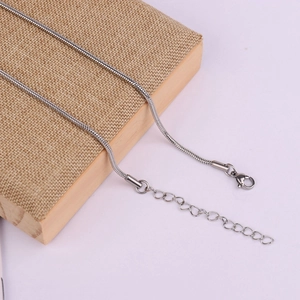 Detailed close-up of stainless steel snake chain necklace with lobster clasp on wood
