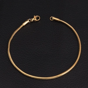 Close-up of golden snake bone chain bracelet with lobster clasp on black background