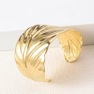 Detailed view of wide golden bangle showing high-polished feather texture and metal craft