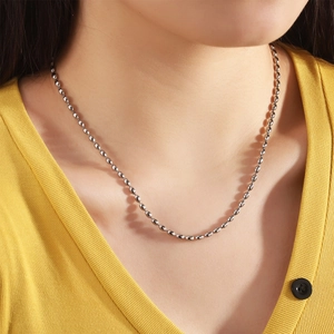 Close-up of polished silver bead chain necklace on a model wearing a yellow sweater