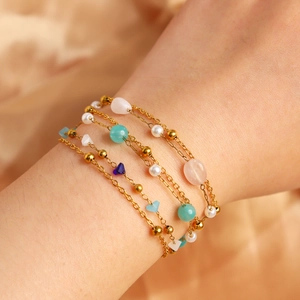 Detail of layered gold bracelet with freshwater pearls and pink gemstone charms