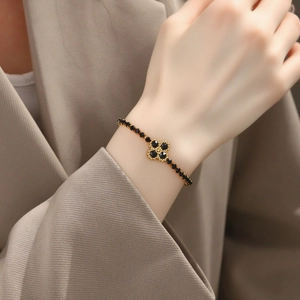 Primer plano de una pulsera de trébol en titanio chapado en oro 18K con piedras negras de mujer