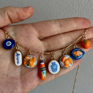 Golden charm necklace with Mediterranean pendants including lemon, evil eye and orange