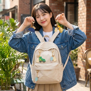 Off-white canvas backpack featuring colorful skate, umbrella, and taxi keychains set outdoors