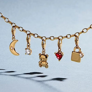 Detalle de dijes de acero inoxidable dorado con luna, oso, corazón y candado en una cadena