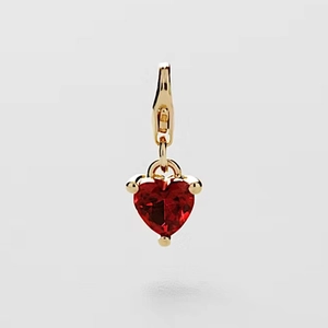 Detalle de un colgante de corazón con piedra roja, acabado dorado y cierre de mosquetón