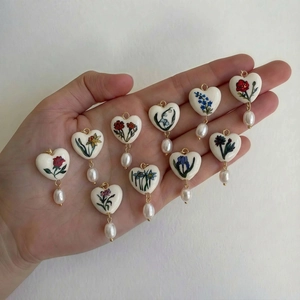 Lot de 10 breloques cœur fleuries avec perles gouttes présentées sur une paume