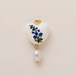 Détail d'un pendentif cœur en céramique avec motif floral bleu et perle blanche