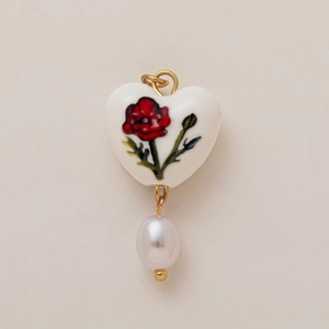 Détail du pendentif en porcelaine en cœur avec motif floral rouge et perle blanche