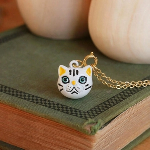 Dettaglio di collana placcata oro 18K con ciondolo a forma di gatto su un libro vintage verde