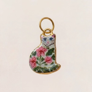 Nahaufnahme des Emaille-Katzenanhängers mit rosa Blumen und blauen Augen auf Goldrahmen