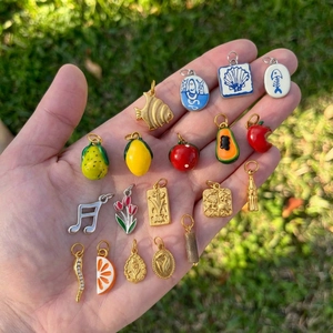 18K gold plated stainless steel fruit and flower charms set held in a hand over grass