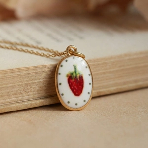 Vintage oval strawberry pendant necklace with gold chain on rustic book background