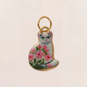Nahaufnahme von Katzenanhänger mit rosa Emaille-Blumen auf Keramik und Gold-Metallrand