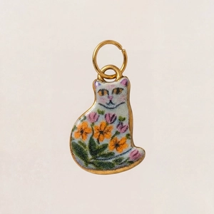 Makro-Detail von goldenem Katzenanhänger mit bunten Emaille-Blumenmustern und Laub