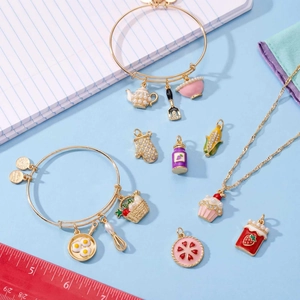 Set gioielli dorati con ciondoli a forma di uovo fritto, cupcake e teiera su sfondo blu