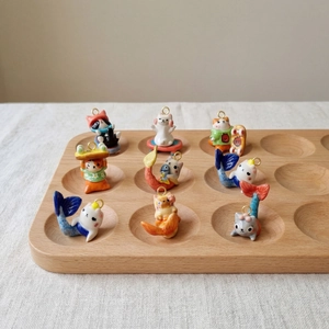Detailansicht von neun bunten handbemalten Keramik-Katzenanhängern auf einem Holztablett