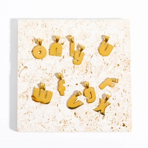 Detailansicht der goldenen Buchstaben-Anhänger mit Zirkonia auf Travertinplatte