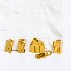 Nahaufnahme von goldenen Buchstabenanhängern aus Edelstahl mit Zirkonia auf Naturstein